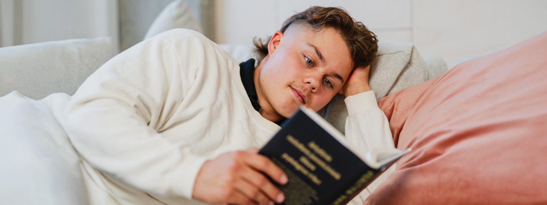 Nuori mies lukee kirjaa s&auml;ngyll&auml;.